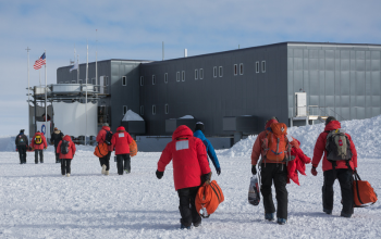 People walking towards a gray building sitting on snow.